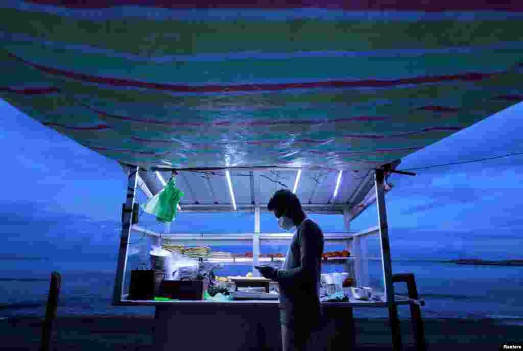 A street vendor wearing a face mask uses his mobile phone while waiting for customers at his food stall near a beach in Colombo, Sri Lanka.