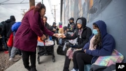 A resident distributes homemade sandwiches to migrants camping on a street in downtown El Paso, Texas, Dec. 18, 2022.