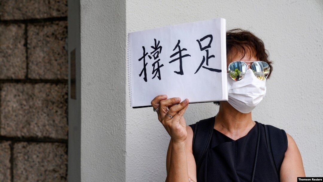 A woman holds up a paper pad that reads "support sibling" while waiting outside the court to bid farewell to a prison van transporting Tong Ying-kit in Hong Kong