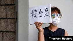 A woman holds up a paper pad that reads "support sibling" while waiting outside the court to bid farewell to a prison van transporting Tong Ying-kit in Hong Kong