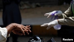 A volunteer of the community emergency response team instructs a man on a motorbike how to sanitize hands following an outbreak of the coronavirus disease, along a road in Karachi, Pakistan, March 21, 2020.