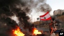 An anti-government protester carries her national flag past burning tires blocking the main highway during protests against the corruption in Khaldeh, south of Beirut, Lebanon, Nov. 13, 2019.