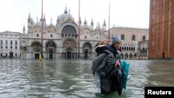  A woman carrying a child on her back wades in the flooded St. Mark's Square in Venice, Italy November 12, 2019. REUTERS