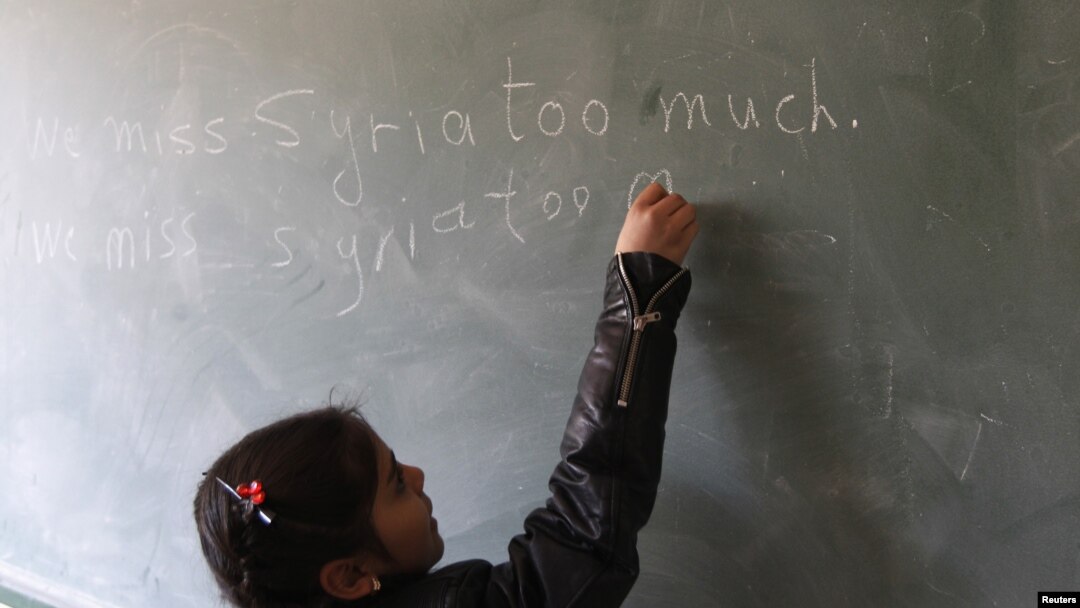 FILE - A Syrian refugee girl writes "we miss Syria too much" on the chalkboard in her classroom in Majdel Anjar in Bekaa Valley December 27, 2012.