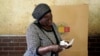 FILE - A woman scrutinizes ballot papers before casting her vote at a polling station in Harare, Zimbabwe, Wednesday, Aug. 23, 2023.