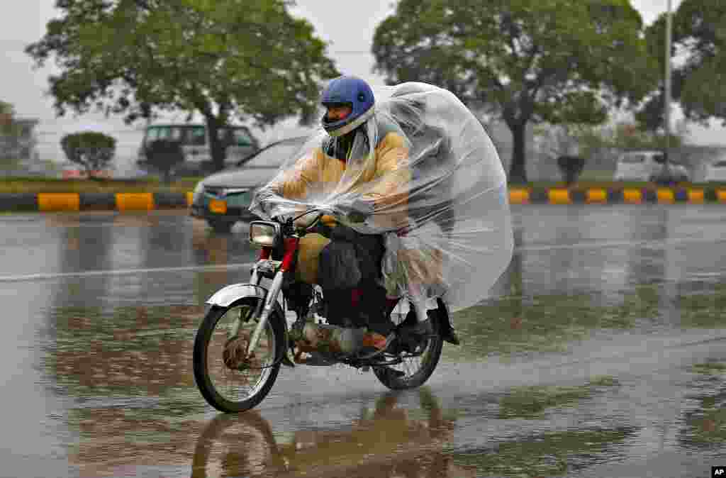 Seorang pengendara sepeda motor dan yang dibonceng, menutupi tubuh mereka dengan lembaran plastik untuk melindungi diri dari hujan di jalan raya di Islamabad, Pakistan. (Foto: AP)