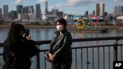 一名戴口罩的游客在东京拍照，背景是奥林匹克运动会标志。2020年1月29日照片