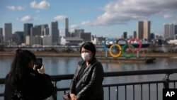 A tourist wearing a mask pauses for photos with the Olympic rings in the background Jan. 29, 2020, in the Odaiba district of Tokyo. 