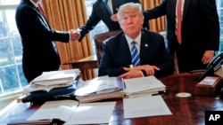Presiden Donald Trump duduk di mejanya setelah pertemuan dengan CEO Intel Brian Krzanich, kiri, dan anggota stafnya di Oval Office Gedung Putih di Washington, 8 Februari 2017. (Foto: AP/Pablo Martinez Monsivais)