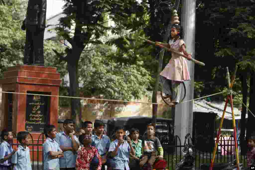 Indian school students watch as a girl performs a rope balancing act for alms, on a street in Hyderabad.