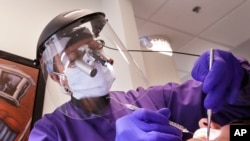 Dentist Dr. Kathleen Saturay wears additional protective equipment, including a face shield and disposable mask over a respirator mask, as she exams a patient in Seattle, May 27, 2020.