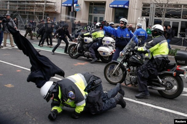 Un policía cae al suelo mientras otro lanza gas pimienta a manifestantes anti-Trump en el centro de Washington.