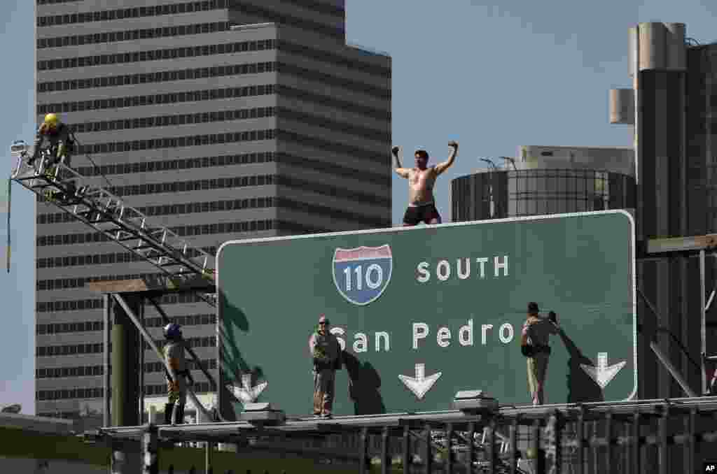California Highway Patrol officers try to coax a man off a freeway sign in downtown Los Angeles, California.