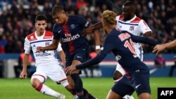 Penyerang Paris Saint-Germain, Kylian Mbappe (dua dari kanan), berebut bola dengan gelandang Lyon, Houssem Aouar (kiri), sementara Neymar, penyerang PSG (kanan) berlari dalam laga liga utama Perancis, L1, antara Paris Saint-Germain dan Olympique de Lyon (OL) pada Minggu, 7 Oktober 2018 di Stadion Parc des Princes di Paris. 