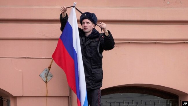 Un oficial de policía ata una cinta de luto a una bandera rusa en San Petersburgo, Rusia, el domingo 24 de marzo de 2024. Rusia celebró un día de luto nacional el domingo, tras el ataque a una sala de conciertos en Moscú.