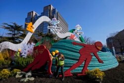 Workers wearing face masks to help protect from the coronavirus set up a decoration for the Winter Olympic Games in Beijing, Jan. 16, 2022.