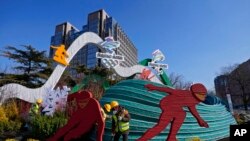 Workers wearing face masks to help protect from the coronavirus set up a decoration for the Winter Olympic Games in Beijing, Jan. 16, 2022. 