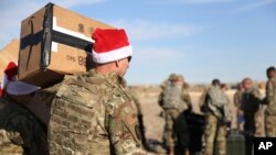 A U.S. soldier carries Christmas gifts from a helicopter to deliver to his comrades on a base near the al-Omar oilfield in eastern Syria, Dec. 23, 2019.