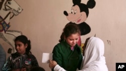 FILE - A woman comforts a child at a community development center in the Manshiet Nasr neighborhood of Cairo, Egypt, Feb. 25, 2015, as a Disney character is seen in the background.