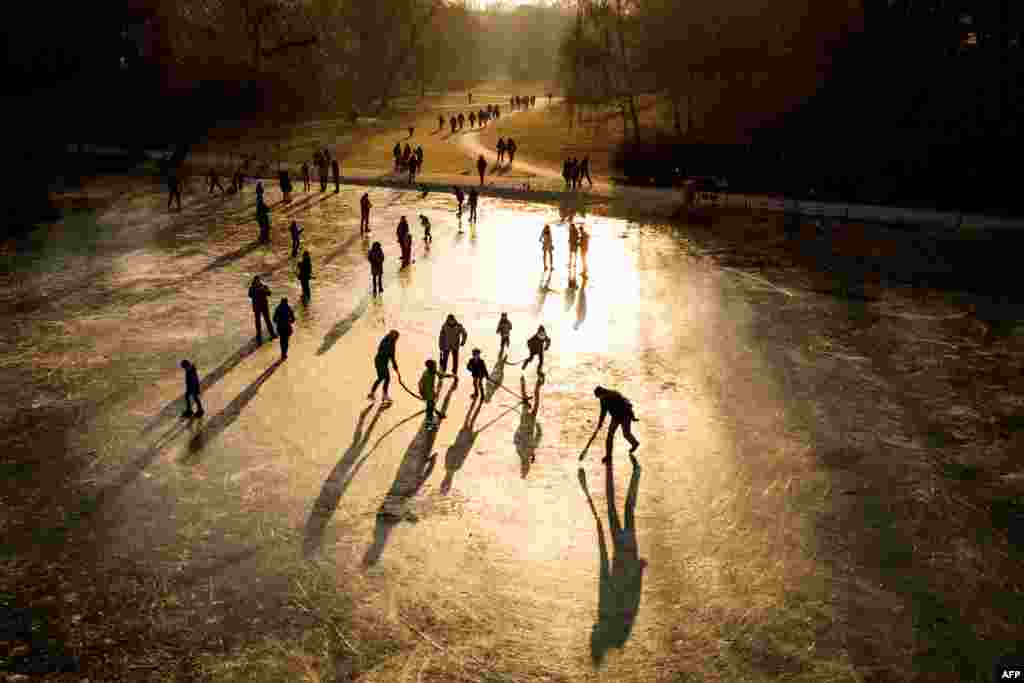 The sun sets as people play on a frozen pond and walk along the paths of a park next to Schoeneberg town hall in Berlin, Germany, March 4, 2018.