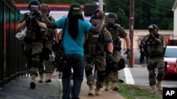 Police wearing riot gear walk toward a man with his hands raised, in Ferguson, Missouri, Aug. 11, 2014.