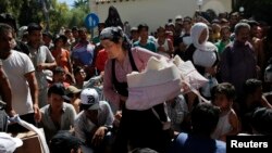 A migrant woman exits the police station carrying her infant baby as other migrants line up for a registration procedure on the Greek island of Kos, Aug. 18, 2015. 