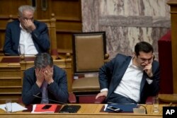 FILE - Greek Finance Minister Euclid Tsakalotos, left, and Greece's Prime Minister Alexis Tsipras, right, react during a parliamentary session to vote on more austerity measures as part of an agreement with international bailout creditors, in Athens, May 18, 2017.