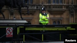 FILE - A police officer stands at a vehicle barrier at the Houses of Parliament, in Westminster, London, Britain, Aug. 15, 2018.