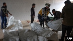 Residents and a rescuer from the Syrian White Helmets pile up bodies of civilians killed in a Syrian government bombardment in the town of Qawqafeen in the rebel-held Idlib province on Nov. 25, 2023.