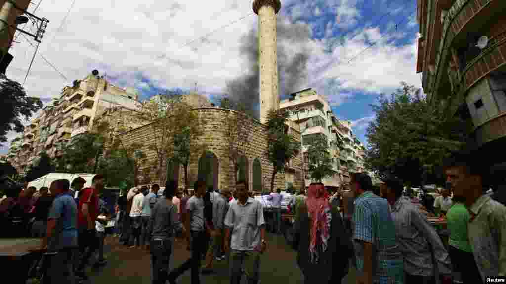 Civilians walk as smoke rises behind a mosque after what activists say was shelling from the Syrian regime in Aleppo&#39;s Bustan al-Qasr district, Sept. 23, 2013.
