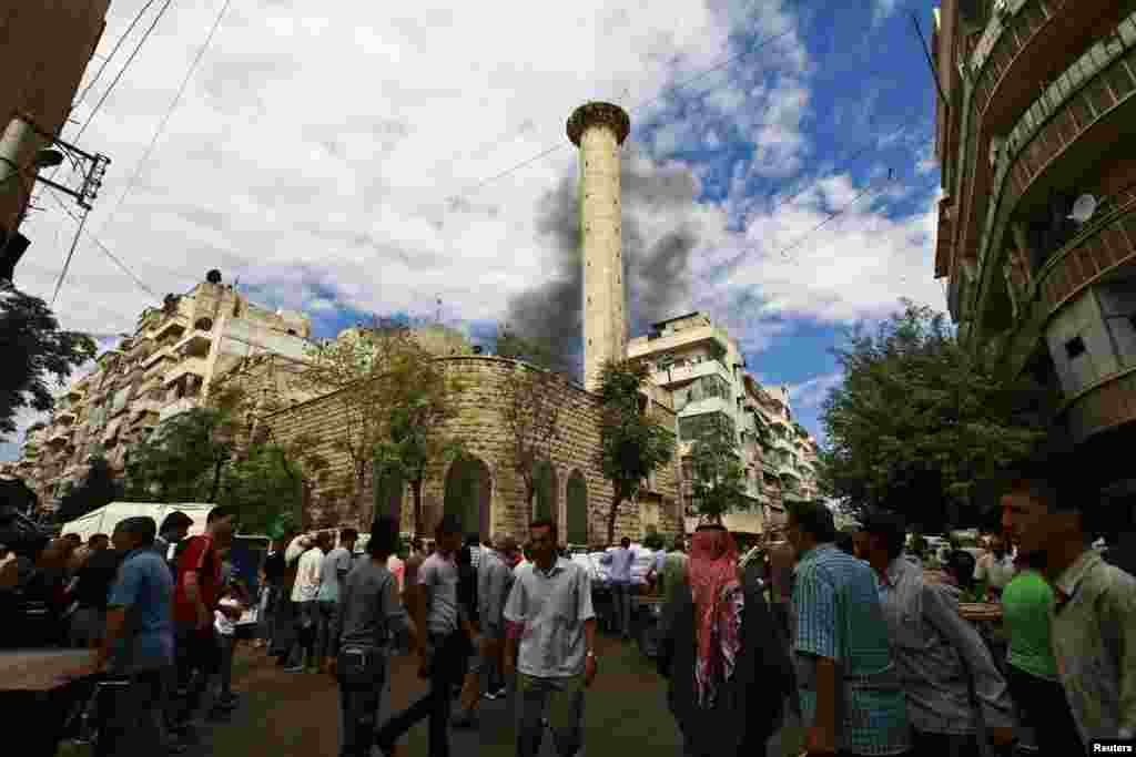 Civilians walk as smoke rises behind a mosque after what activists say was shelling from the Syrian regime in Aleppo's Bustan al-Qasr district, Sept. 23, 2013.