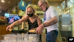 Coffee shop owner Yiannis Tzikas and his wife Kaiti Drimba pour champagne into plastic glasses after the Milwaukee Bucks win the NBA title, in the Sepolia district of Athens on Wednesday, July 21, 2021. (AP Photo/Derek Gatopoulos)
