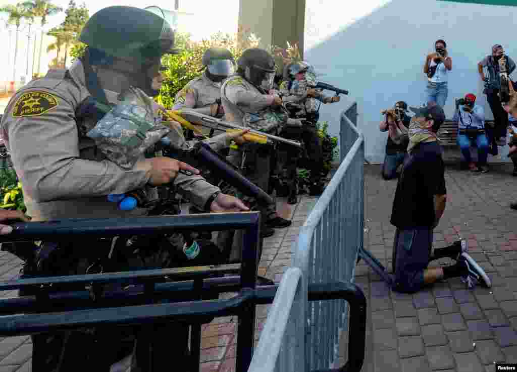 A demonstrator kneels as Los Angeles County sheriff&#39;s deputies prepare to fire pepper balls, flash-bangs and rubber bullets in a protest against the death of 18-year-old Andres Guardado and racial injustice, in Compton, California, June 21, 2020.