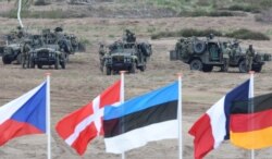 FILE - Flags wave in front of soldiers who take positions with their army vehicles during the NATO exercises near Swietoszow Zagan, Poland, June 18, 2015.