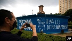 FILE - A pedestrian takes a photo of graffiti on a temporary metal barrier set up to protect the perimeter of the Christopher Columbus statue which was removed by authorities on Paseo de la Reforma in Mexico City, Oct. 12, 2020.