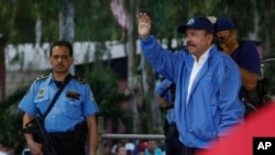 Escoltado por uno de sus guardias de seguridad armados, Daniel Ortega, a la derecha, saluda a una multitud de fieles del partido durante una marcha por la paz, en Managua, Nicaragua, el 7 de julio de 2018. 