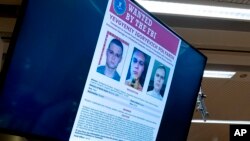 Russian Yevgeniy Polyanin, wanted by the FBI, is displayed on monitors as Attorney General Merrick Garland accompanied by Deputy Attorney General Lisa Monaco. (File)