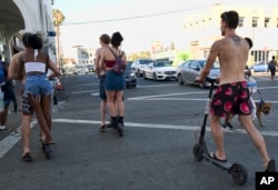 In this July 24, 2018, file photo, riders make their way across a street on electric scooters in the Venice Beach section of Los Angeles.