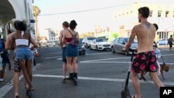 FILE - In this July 24, 2018, file photo, riders make their way across a street on Bird electric scooters in the Venice Beach section of Los Angeles.