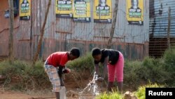 Children collect water from a communal tap beneath election posters for President Jacob Zuma's African National Congress (ANC) in Bekkersdal township south of Johannesburg, May 3, 2014. 