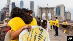 Friends stop and hug for a moment as hundreds of COVID survivors march across the Brooklyn Bridge, Aug. 7, 2021, in New York. The U.S. is now averaging thousands of new COVID-19 infections a day. 