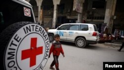 FILE - A Syrian child walks near an International Red Cross vehicle in the rebel-held city of Douma, in the eastern Damascus suburb of Ghouta, Syria, Nov. 12, 2017. 