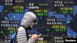A man walks past an electronic board displaying various countries' stock price indices outside a brokerage in Tokyo, Japan, Mar. 14, 2014.