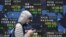 A man walks past an electronic board displaying various countries' stock price indices outside a brokerage in Tokyo, Japan, Mar. 14, 2014.