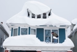 FILE - A man shovels snow from the roof of his home after a storm in Buffalo, N.Y., Nov. 20, 2014.