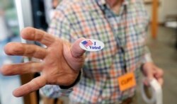 Cliff Smith, a Ridgeland, Mississippi, poll worker, offers a voter an "I Voted" sticker after they cast their ballot, Nov. 5, 2019.