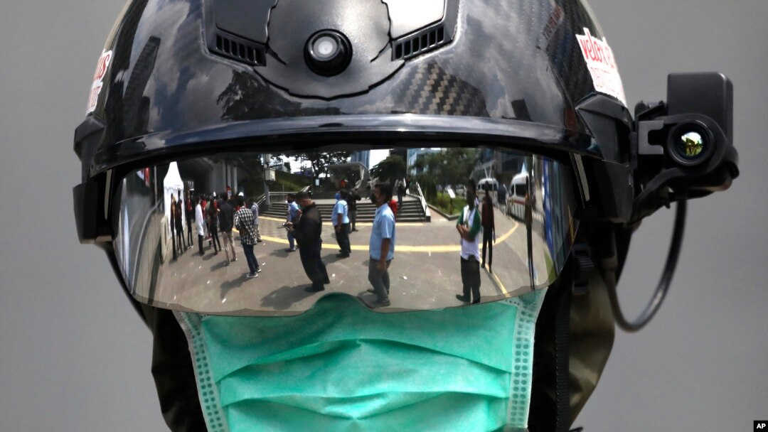 Antrean warga untuk dites Covid-19 terlihat memantul dari kaca pelindung wajah seorang petugas medis di luar mobil keliling "uji cepat Coid-19" di Jakarta, 6 Mei 2020.
