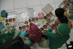 Para siswa sebuah sekolah di Jakarta, duduk di lantai sebelum menyantap makanan mereka saat peluncuran program makanan gratis , Senin, 6 Januari 2025. (Achmad Ibrahim/AP)