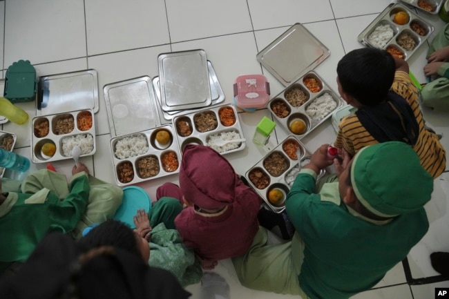 Para siswa sebuah sekolah di Jakarta, duduk di lantai sebelum menyantap makanan mereka saat peluncuran program makanan gratis , Senin, 6 Januari 2025. (Achmad Ibrahim/AP)