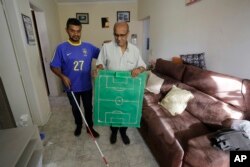 Carlos Junior prepares to leave his home with the help of his father Carlos Santana, who carries a model soccer field that will be used to help him follow the live broadcast of the World Cup match between Brazil and Mexico.
